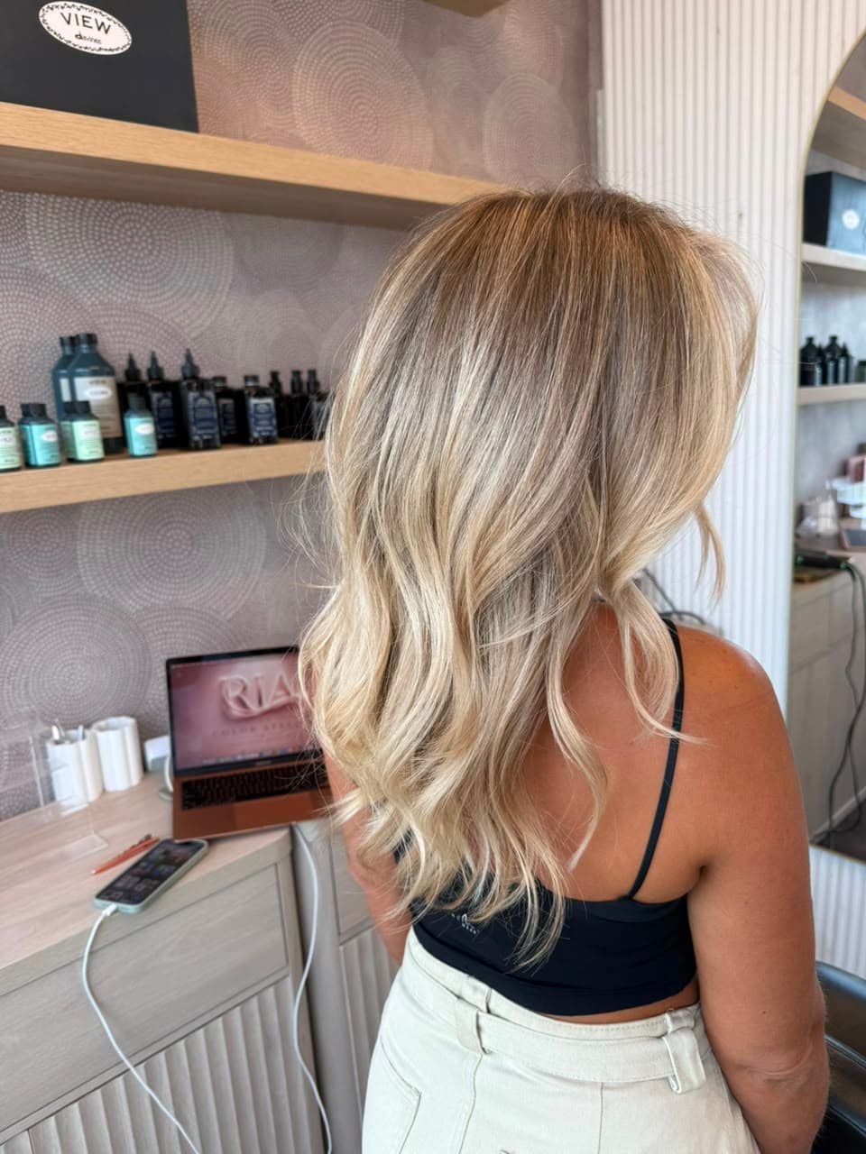 Client with soft blonde balayage in the atelier, Davines products on the shelf behind