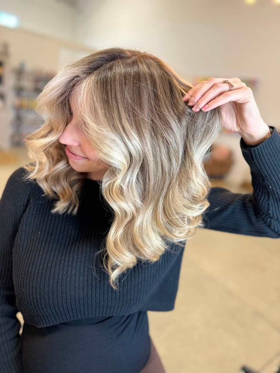Client running her hand through blonde balayage waves with a soft root